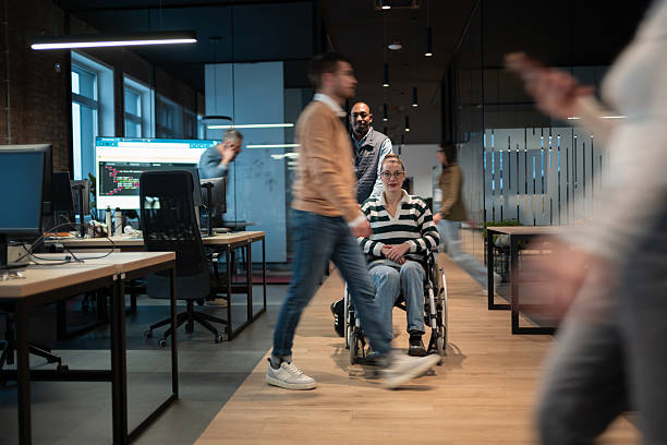istock Wheelchair accessibility and inclusion in a startup open space office. A man assists a colleague in a wheelchair while others collaborate, business people, teamwork, innovation and diversity concept 2207234687