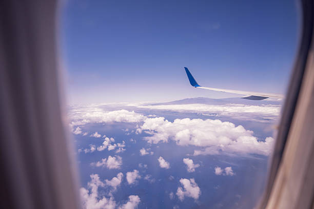 Hawaiian, United States - June 24 2024:This photo was taken aboard a Hawaiian Airlines flight as it approached the Big Island of Hawaii. The aircraft was descending through a dreamy sky painted with soft pastel clouds during sunset. The iconic red wingtip of Hawaiian Airlines stands out against the glowing horizon, signaling the arrival to the tropical paradise. The peaceful cloudscape and warm light capture the beauty and excitement of finally reaching Hawaii