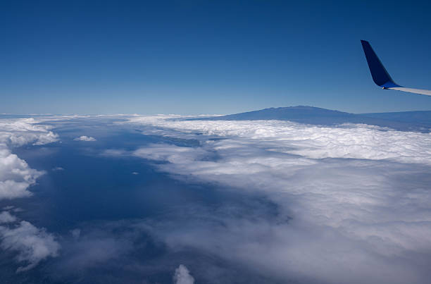 Hawaiian, United States - June 24 2024:This photo was taken aboard a Hawaiian Airlines flight as it approached the Big Island of Hawaii. The aircraft was descending through a dreamy sky painted with soft pastel clouds during sunset. The iconic red wingtip of Hawaiian Airlines stands out against the glowing horizon, signaling the arrival to the tropical paradise. The peaceful cloudscape and warm light capture the beauty and excitement of finally reaching Hawaii