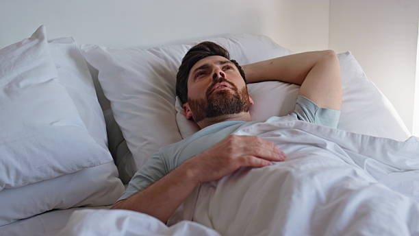 istock Lazy guy awaking bed enjoying sunny weekend morning closeup. Brunette waking up 2207238046