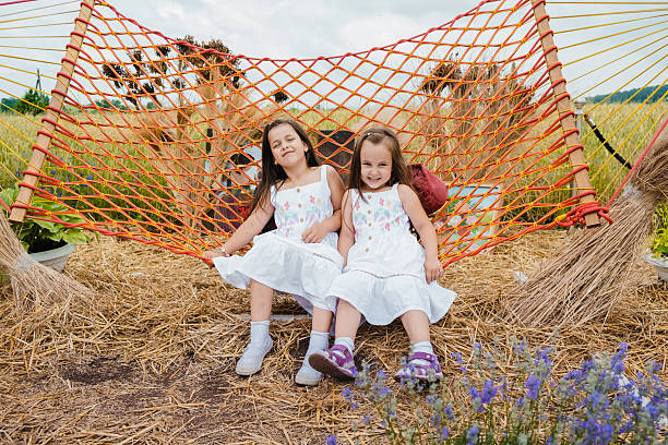 istock Two girls in white dresses are joyfully swinging on a red mesh hammock 2207238190