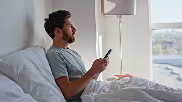 istock Awake guy scrolling smartphone in bed early morning. Relaxed brunette messaging 2207239926