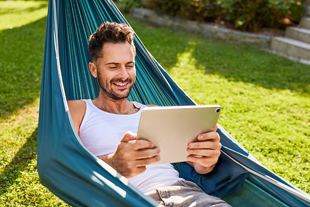 istock Adult man in hammock using digital tablet relaxing in backyard 2207240874