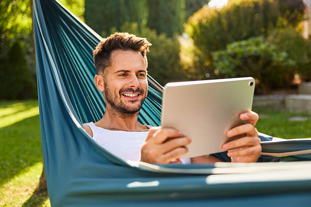 istock Smiling adult man using digital tablet in backyard resting in hammock 2207240886