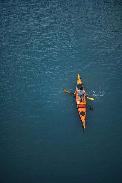 istock Person Kayaking on Calm Blue River in a Bright Orange Kayak 2207242179