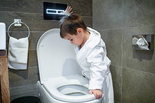 istock Happy boy in the bathroom, wearing bathrobe flushing toilet 2207243020
