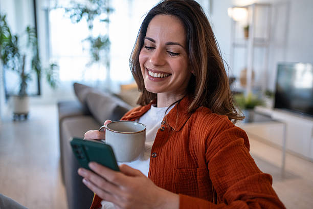 istock Smiling woman relaxing on sofa with coffee and smartphone 2207244121