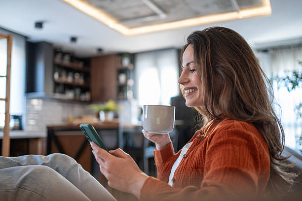 istock Smiling woman relaxing on sofa, enjoying coffee and browsing smartphone at home 2207244140