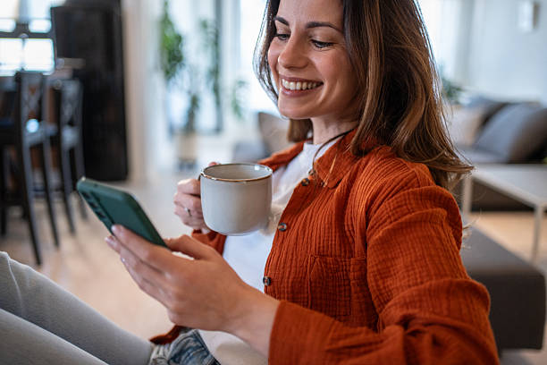 istock Woman relaxing on sofa, enjoying coffee and browsing smartphone at home 2207244154