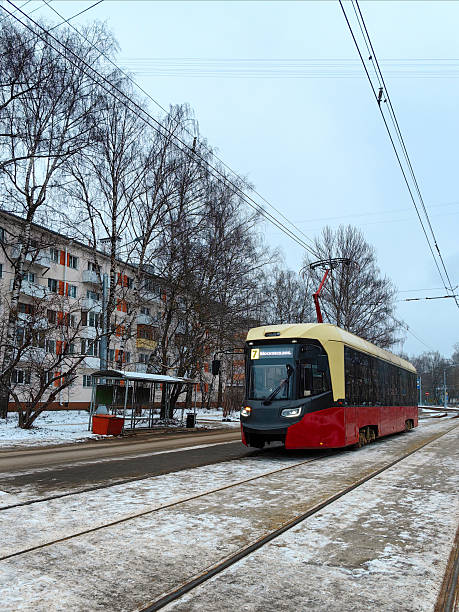 tramvaj a lidé na zastávce na ulici s béžovými pětipatrovými domy s balkony, břízami, stromy a keři. sovětské budovy. zima. rusko.nižnij novgorod.ulice baranova. únor 2025.fotografie. - ručně barvený fotky - stock snímky, obrázky a fotky