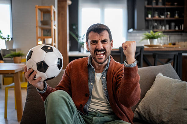 istock Excited soccer fan celebrating goal while watching match at home 2207250332
