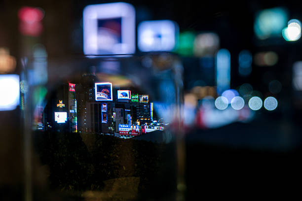 Blurred neon lights reflect off a window in an urban environment at night, captured with a shallow depth of field. The soft focus and colorful tones convey a cinematic, moody city atmosphere