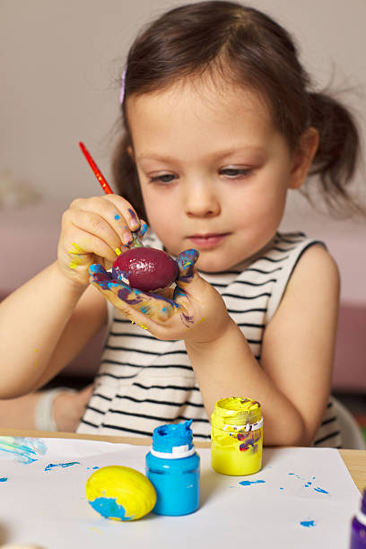 Little child girl paint Easter eggs at home. kid is preparing for Easter.
