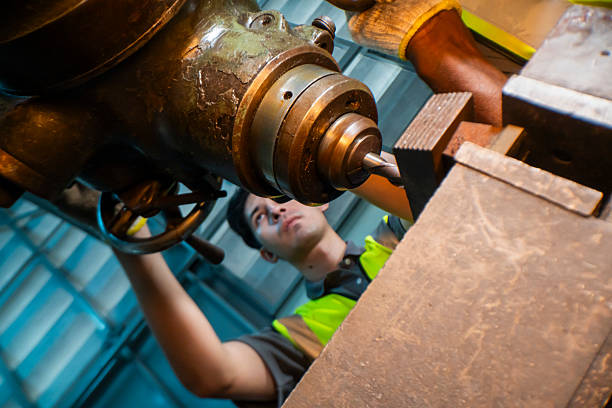 Focused industrial worker operating a heavy-duty drill in a workshop. The image captures precision, skill, and attention to detail, as well as the importance of safety equipment like gloves and vests.