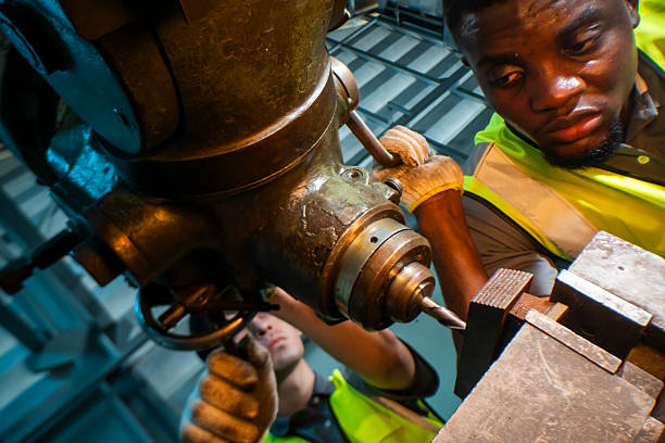 Focused industrial worker operating a heavy-duty drill in a workshop. The image captures precision, skill, and attention to detail, as well as the importance of safety equipment like gloves and vests.