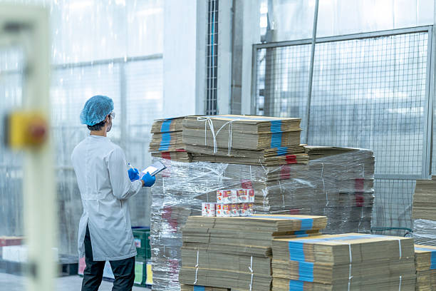 istock A food processing supervisor in protective gear inspecting packaging materials in a factory, holding a clipboard, emphasizing quality control, hygiene, and safety in food production operations 2207257963