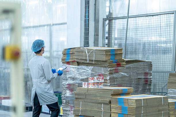 istock A food processing supervisor in protective gear inspecting packaging materials in a factory, holding a clipboard, emphasizing quality control, hygiene, and safety in food production operations 2207258556