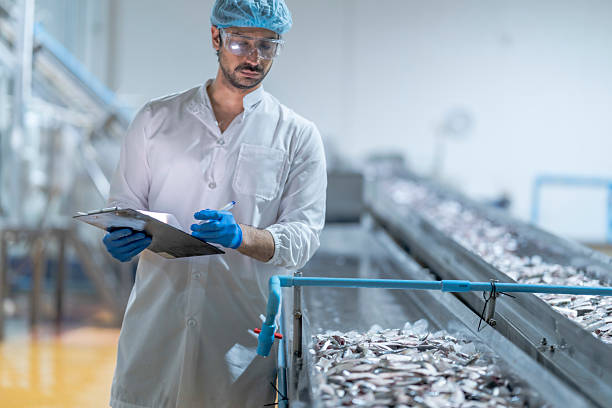 istock A food processing supervisor in protective gear inspecting packaging materials in a factory, holding a clipboard, emphasizing quality control, hygiene, and safety in food production operations 2207258658