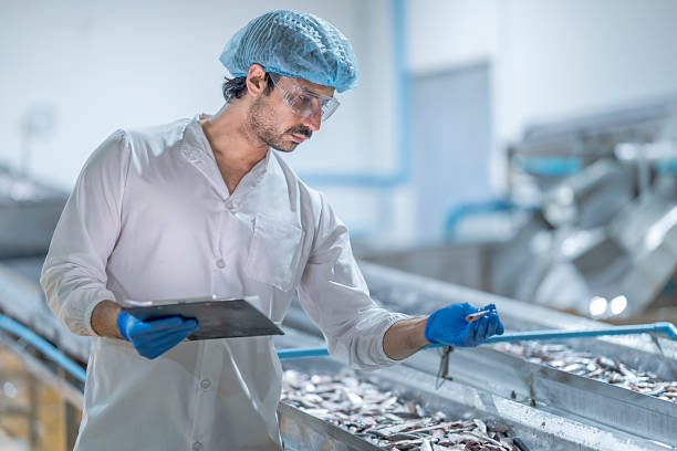 istock A food processing supervisor in protective gear inspecting packaging materials in a factory, holding a clipboard, emphasizing quality control, hygiene, and safety in food production operations 2207259201