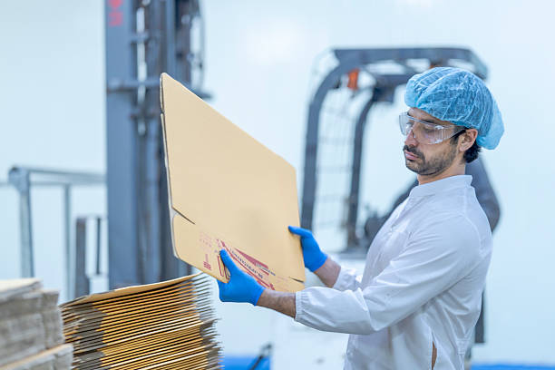 istock A food processing supervisor in protective gear inspecting packaging materials in a factory, holding a clipboard, emphasizing quality control, hygiene, and safety in food production operations 2207259358