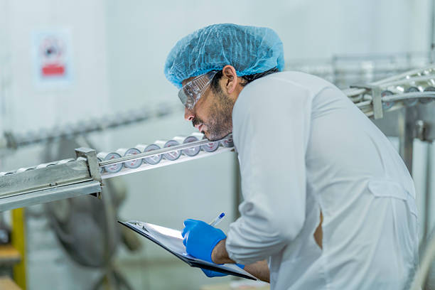 istock A food processing supervisor wearing protective gear and holding a clipboard, inspecting machinery on a production line, emphasizing quality control, safety, and efficiency in industrial operations. 2207261780