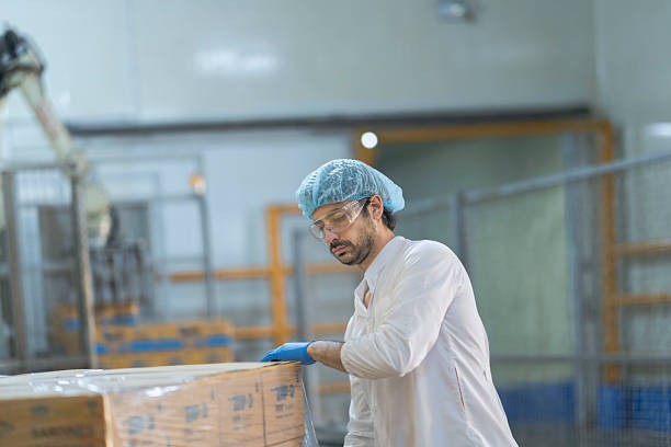 istock A food processing supervisor in protective gear inspecting packaging materials in a factory, holding a clipboard, emphasizing quality control, hygiene, and safety in food production operations 2207262605