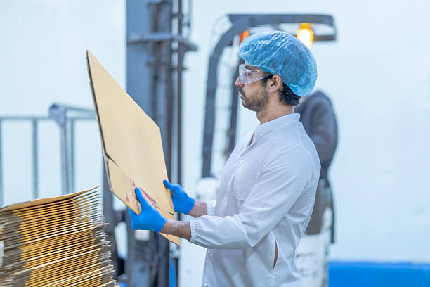 istock A food processing supervisor in protective gear inspecting packaging materials in a factory, holding a clipboard, emphasizing quality control, hygiene, and safety in food production operations 2207262681