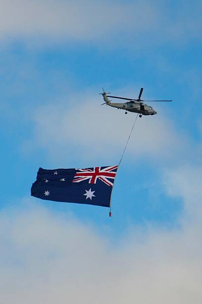istock S-70B Seahawk Helicopter flying over Melbourne with a Australian flag below 2207263156