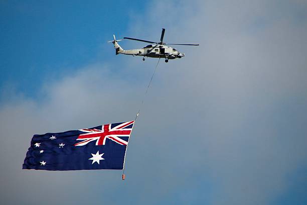 istock S-70B Seahawk Helicopter flying over Melbourne with a Australian flag below 2207263172