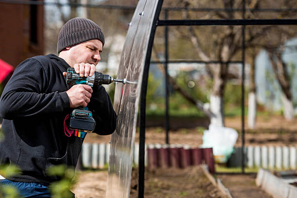 istock A man holds a battery-powered screwdriver and assembles a new greenhouse made of polyethylene, polycarbonate. Macro photography. Side view. Preparing for the spring garden season. 2207264773
