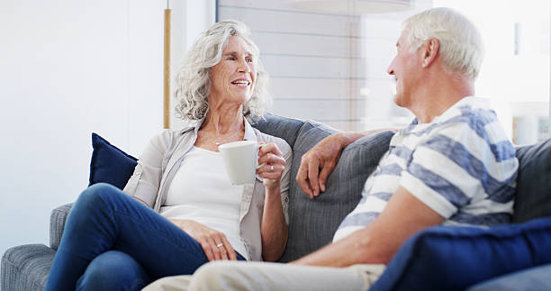 istock Bonding, smile and senior couple with coffee, conversation and romance for relationship in living room. House, old man and woman with tea, retirement and elderly people in lounge, talking or marriage 2207265468