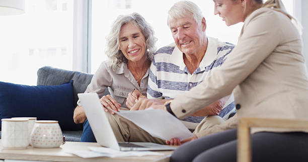 istock Senior couple, accountant and documents with laptop for retirement plan, annuity or insurance on sofa. Elderly man, woman or financial advisor with paperwork for discussion on pension funds or assets 2207265572