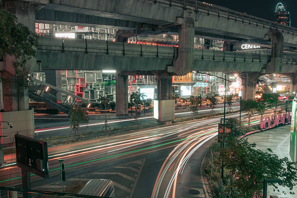 Night light trails at MBK, Thailand, highlight Bangkok's vibrant energy with glowing streets and dynamic vehicle lights.
