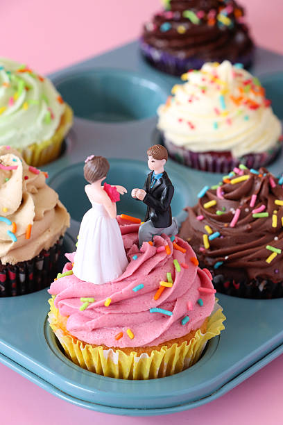 Image of pink muffin tray with wedding cupcake toppers of bride, groom, butter icing, cream /  wedding cakes and muffins