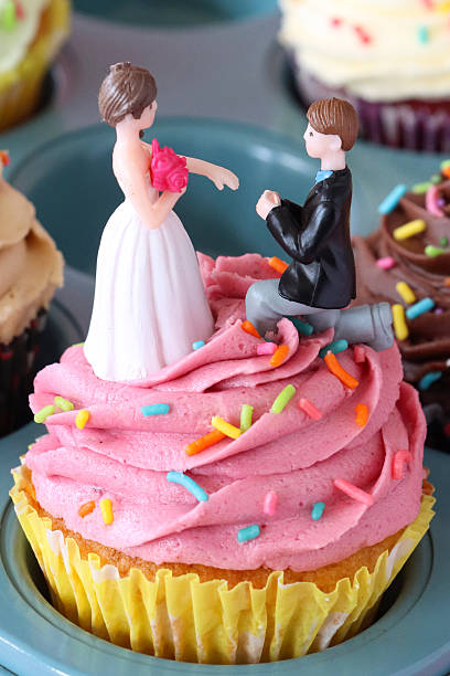Image of pink muffin tray filled with wedding-themed cupcakes, each topped with bride, groom figurines