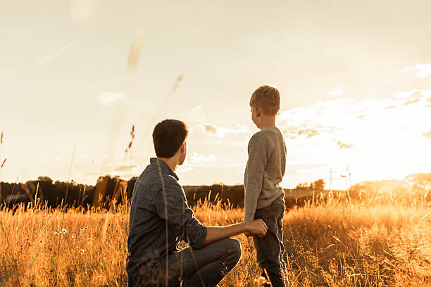 istock Father and son in the meadow watching sunset together. 2207293435