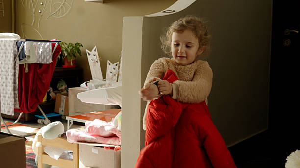 Child, learning to get dressed in cozy home, engages in dressing up with her red winter jacket in front of the mirror fostering her cognitive skill development.