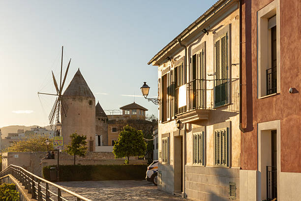 Charming street in Palma de Mallorca featuring a traditional windmill and historic buildings at golden hour.