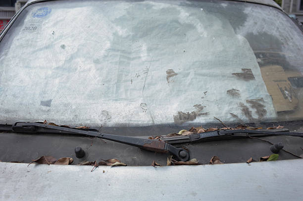 istock Front view of an abandoned silver car, fallen dry leaves on windscreen wiper, sunlight shines onto dirty windshield. 2207298409