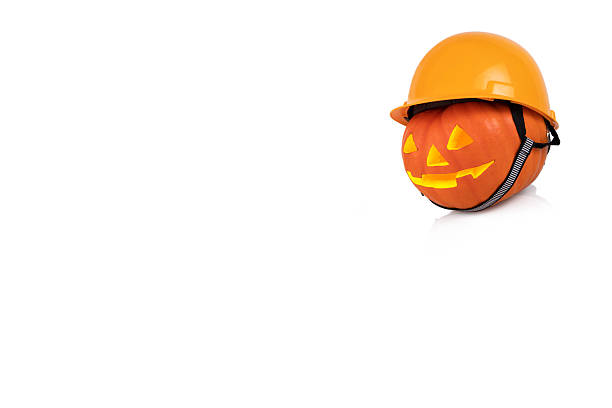 istock Orange pumpkin with glowing eyes in yellow construction helmet. Safety concept. White background. Copy space 2207301212