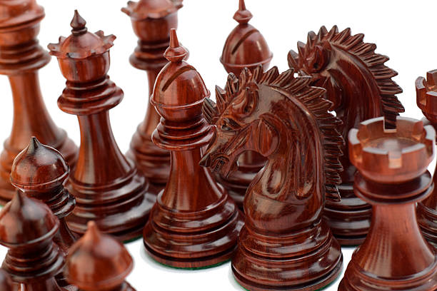 A close-up of intricately carved chess pieces made from rare red padauk wood. The rich, warm hues highlight the fine craftsmanship of the knights, bishop, rook, queen, and pawns