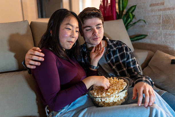 istock Young multiethnic couple watching movie and eating popcorn on sofa 2207309630