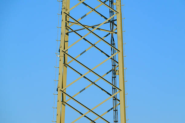 High Voltage electricyty transmission towers with power lines an a blue sky and clouds in the background.