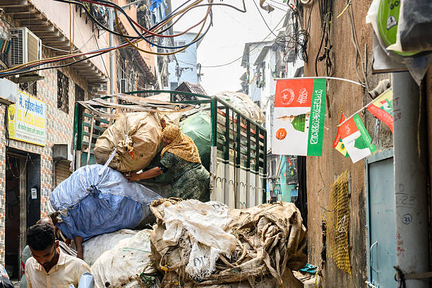 Mumbai, India - November 16, 2024:  woman unloading sacks with waste to recycle from truck on street in  Dharavi slum in Mumbai