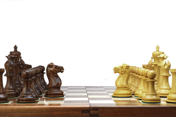 The image captures a close-up of a chessboard from a low angle, showcasing intricately carved wooden chess pieces placed on the board. The pieces, including two horses (knights), stand on the brown and white squares of the chessboard, highlighting the detailed craftsmanship. The board and figures are made of wood.