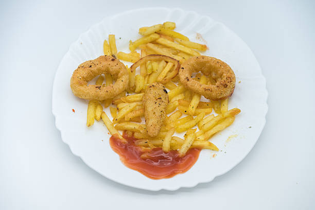 An Asian Chinese woman eating fish and chips meal using kitchen knife and fork in a cafe