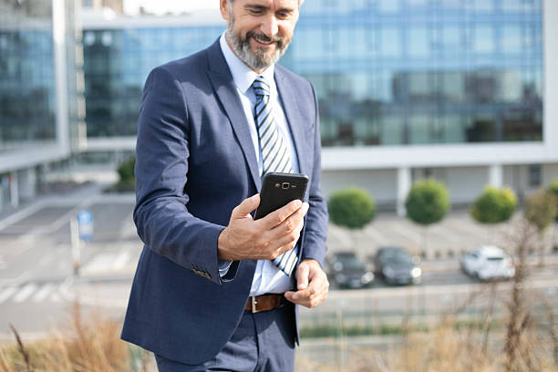 istock Middle-Aged Bearded Businessman with Smartphone in Front of Office Building 2207315833