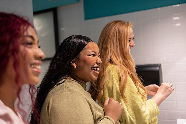 Three young women laughing together in a public restroom