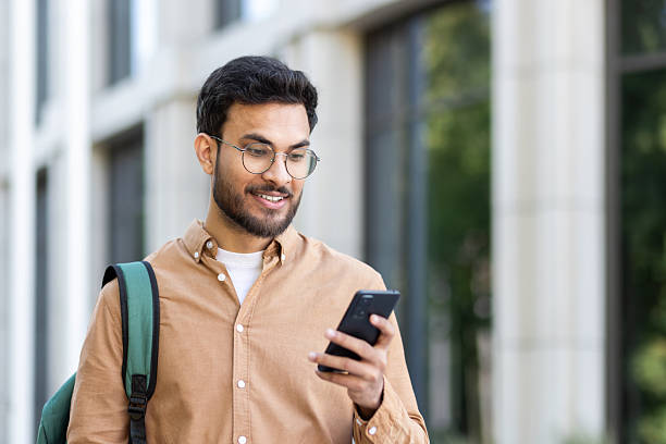 istock Joyful and happy student walking with phone in hands and backpack, man typing text message and browsing social media 2207319190