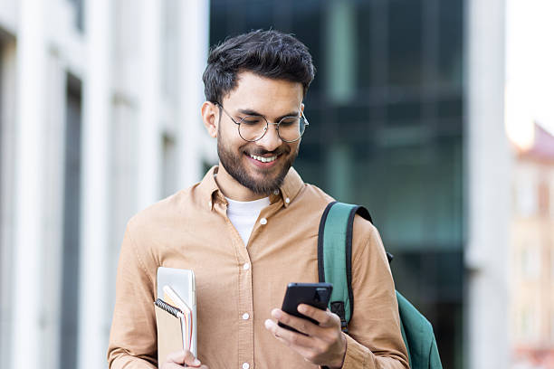 istock Smiling student with backpack and books checks his mobile phone while on campus, showcasing connectivity and modern education. 2207319202